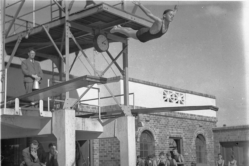 A black and white photo of a boy mid air with the diving board behind him
