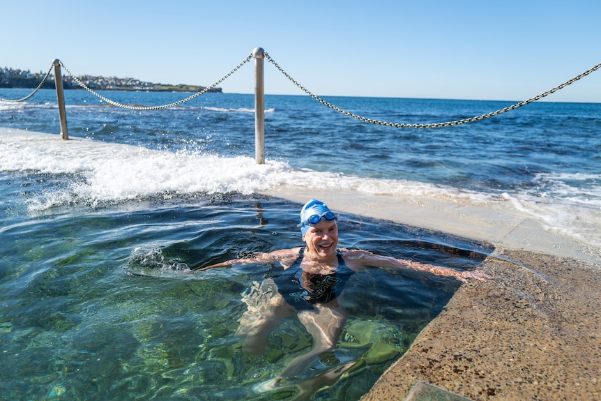 A person in the water with a swimming cap and goggles with the ocean behind her