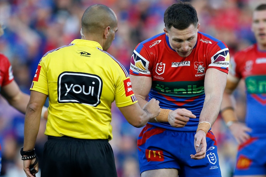 An NRL player points at his arm, telling the referee he was bitten