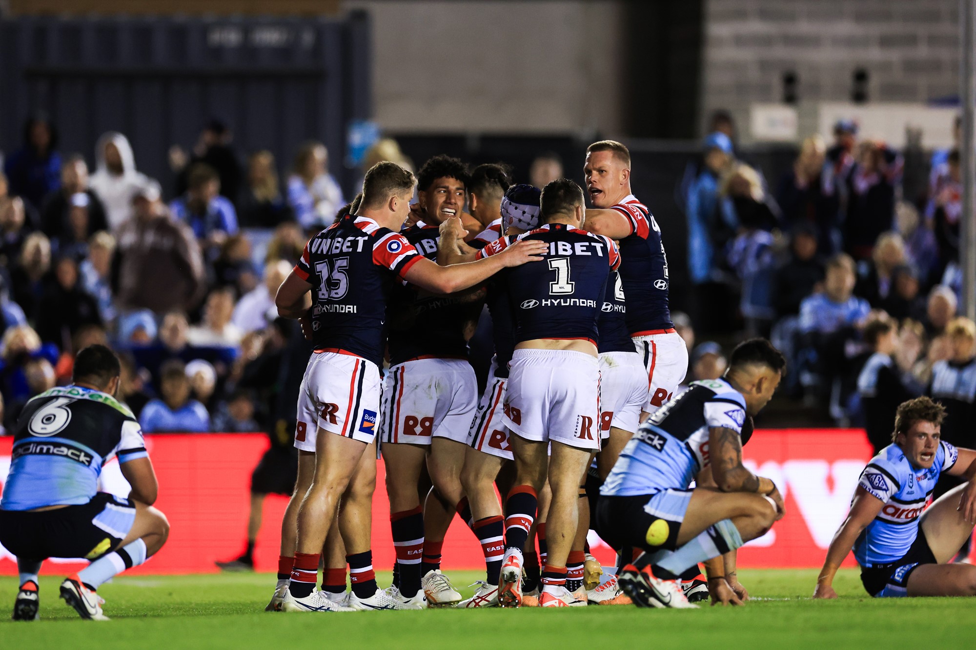 Roosters players hug as Sharks players slump to the grass.