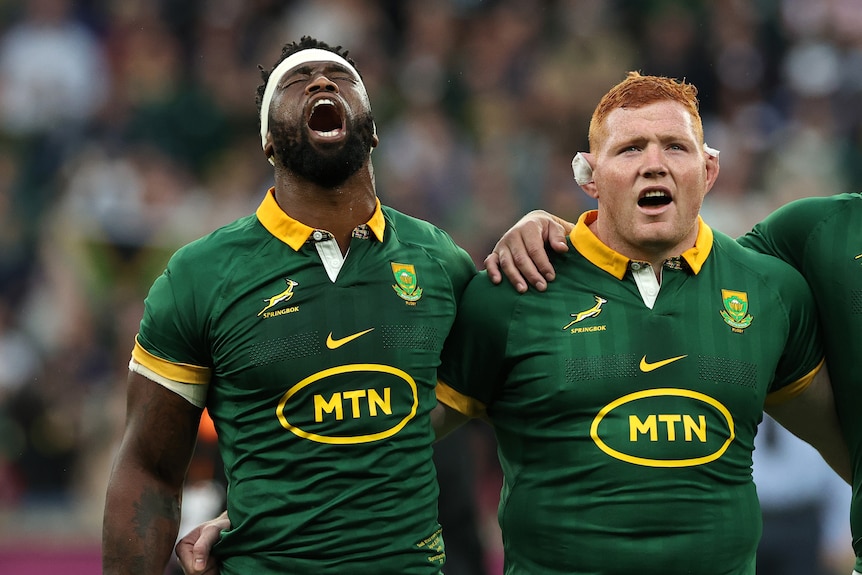 Siya Kolisi sings the national anthem with his eyes closed, arm in arm with a teammate